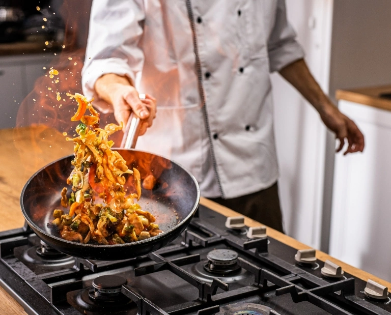 Kucharz podrzucający jedzenie na&nbsp;patelni